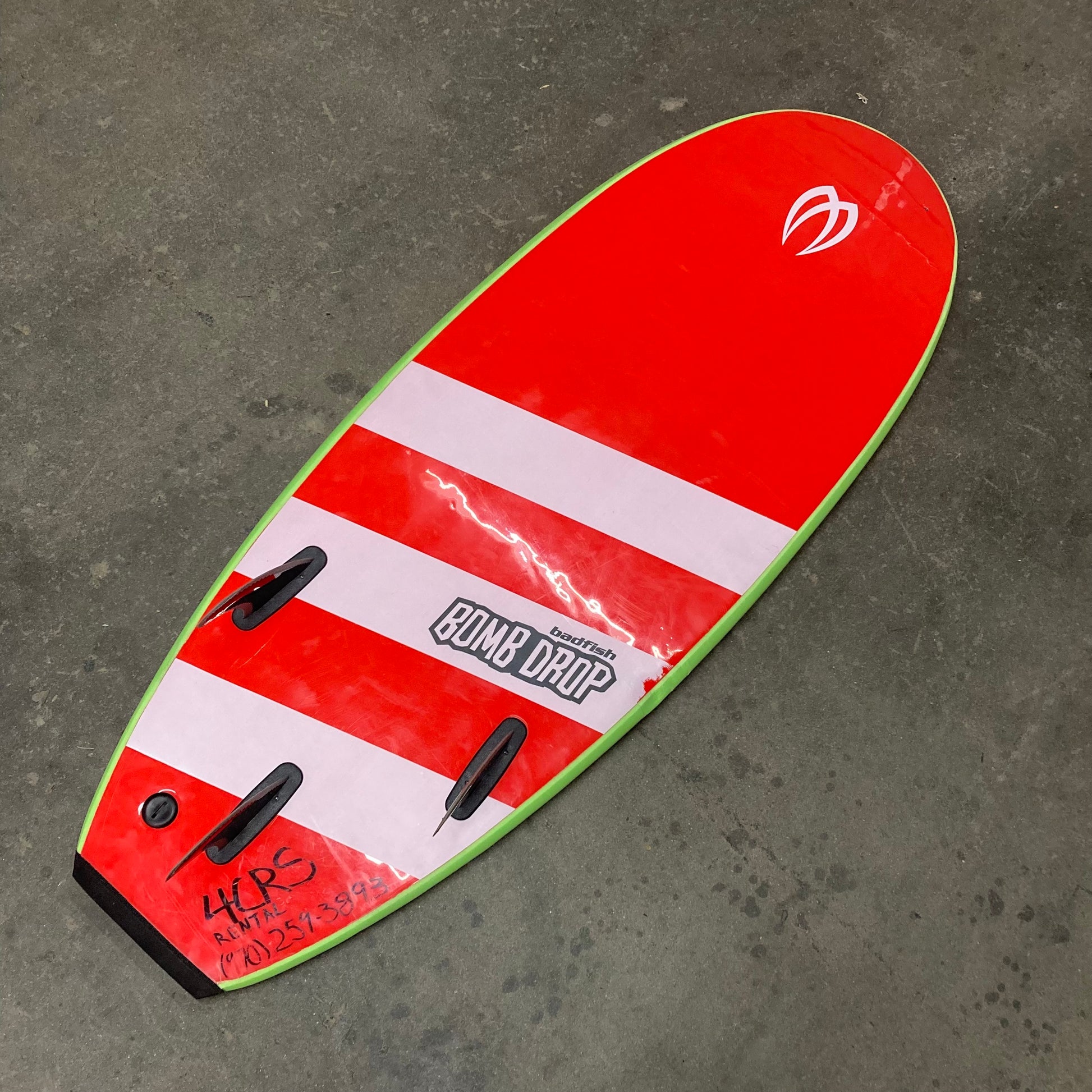 A red and white Demo Bomb Drop surfboard sitting on a concrete floor (brand: Badfish).