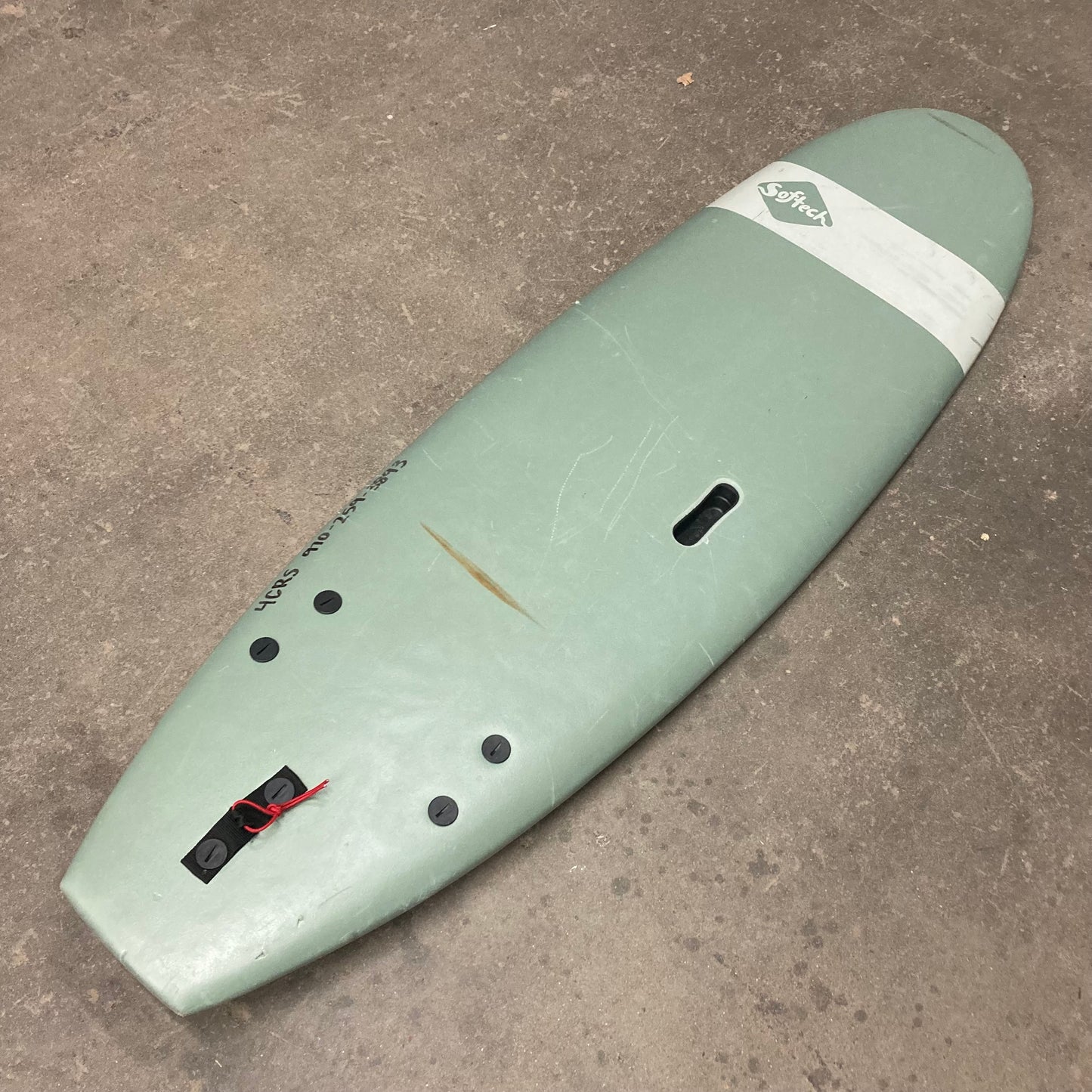 A green Demo Roller surfboard sitting on a concrete floor.