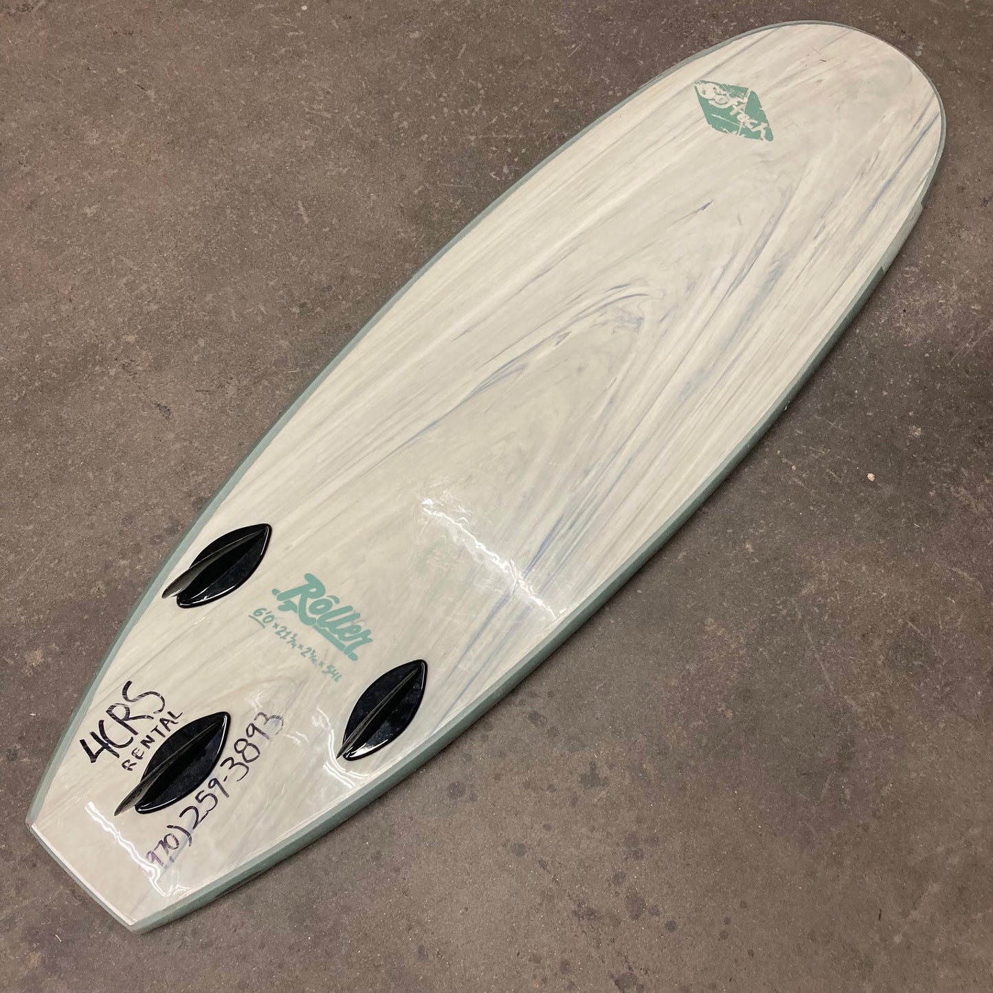 A white Demo Roller surfboard sitting on a concrete floor.