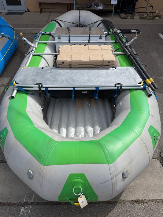 A Demo Rio Craft 16' Package raft by Rio Craft in gray and green, equipped with oars and stacked tan bricks on an NRS Frame, is set on a paved surface.
