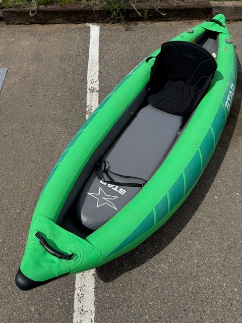 A green Demo STAR Raven Solo inflatable kayak by NRS with a black seat is on a paved surface beside a white line.