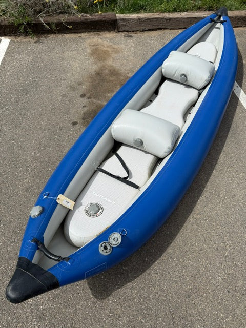Used Demo STAR Outlaw IK Tandem inflatable kayak by NRS with two gray seats and a foot pump valve, shown on a paved surface near a parking space.