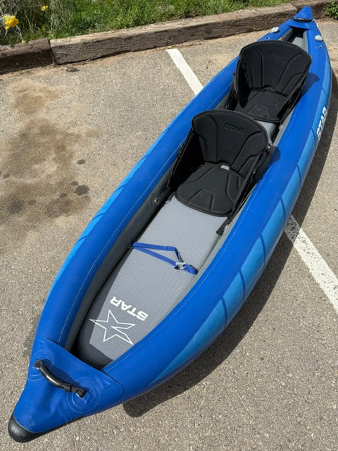A blue Demo STAR Raven Tandem by NRS, featuring two black seats and part of our demo fleet, is placed on an asphalt surface near a parking curb.