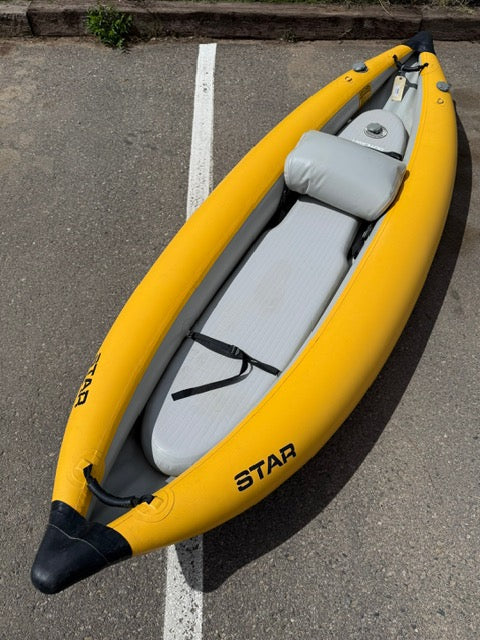 A yellow NRS Demo Outlaw IK Solo from our demo fleet, with a gray seat and paddle strap, rests on asphalt partially over a white parking line.