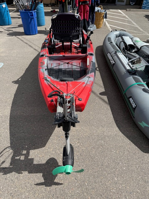 A used Jackson Kayak Liska 12'1 with a Newport NK300 motor is displayed outdoors beside an inflatable boat.
