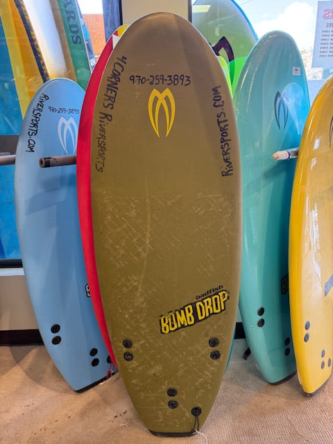 A Badfish Demo Bomb Drop river surfboard from the demo fleet is displayed upright in a surf shop, surrounded by other colorful boards.