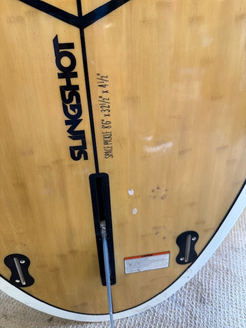 Close-up of a Consignment Slingshot Space Pickle SUP from 4Corners Riversports, showing the logo, model name "Space Pickle 6'6" x 32 1/2" x 4 1/2"", and part of the fin box.
