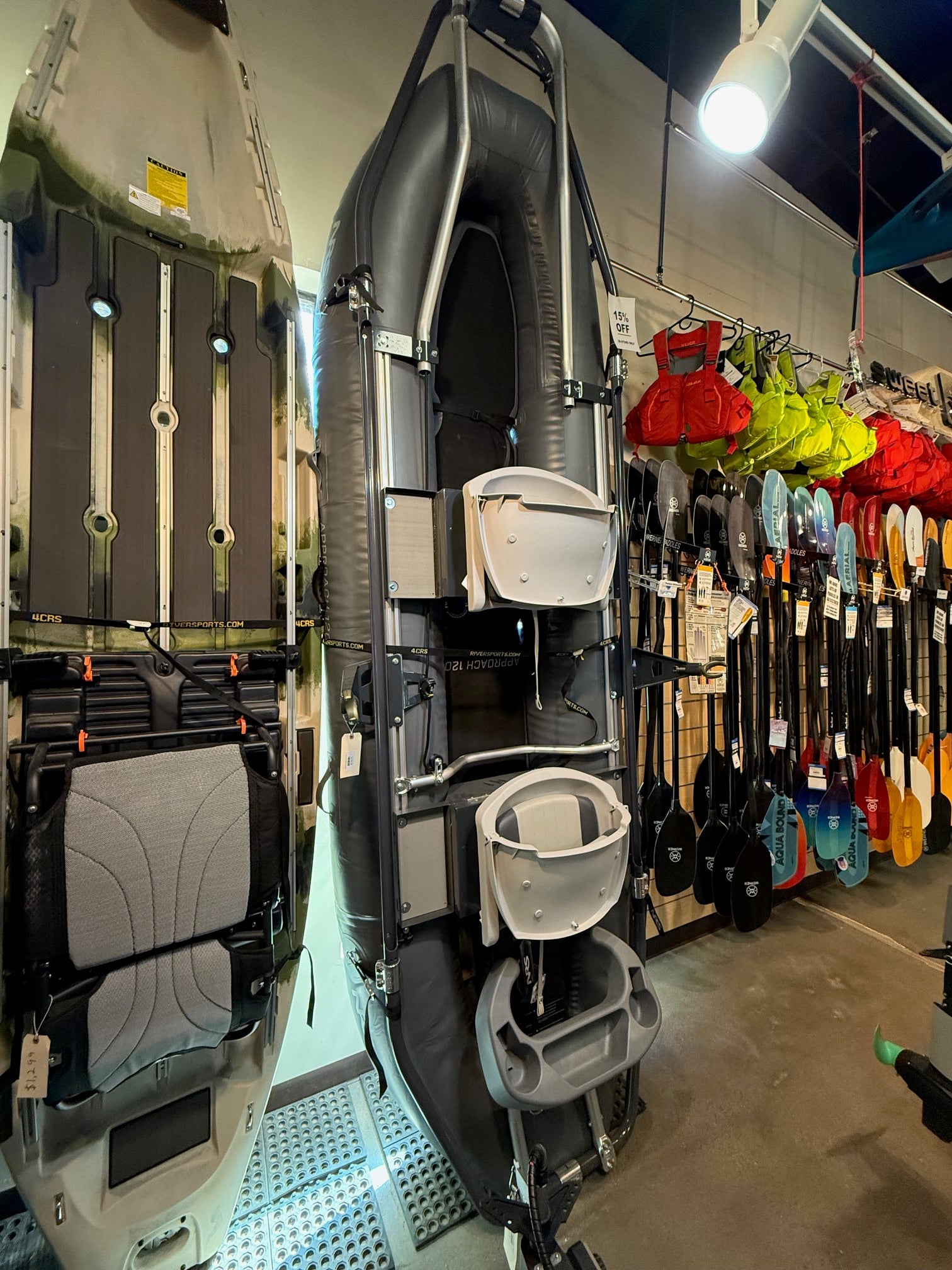 The NRS Approach Fishing Raft - Floor Model is displayed upright in-store, surrounded by paddles and kayaking gear, highlighting this lightweight fishing raft alongside other micro-rafts.