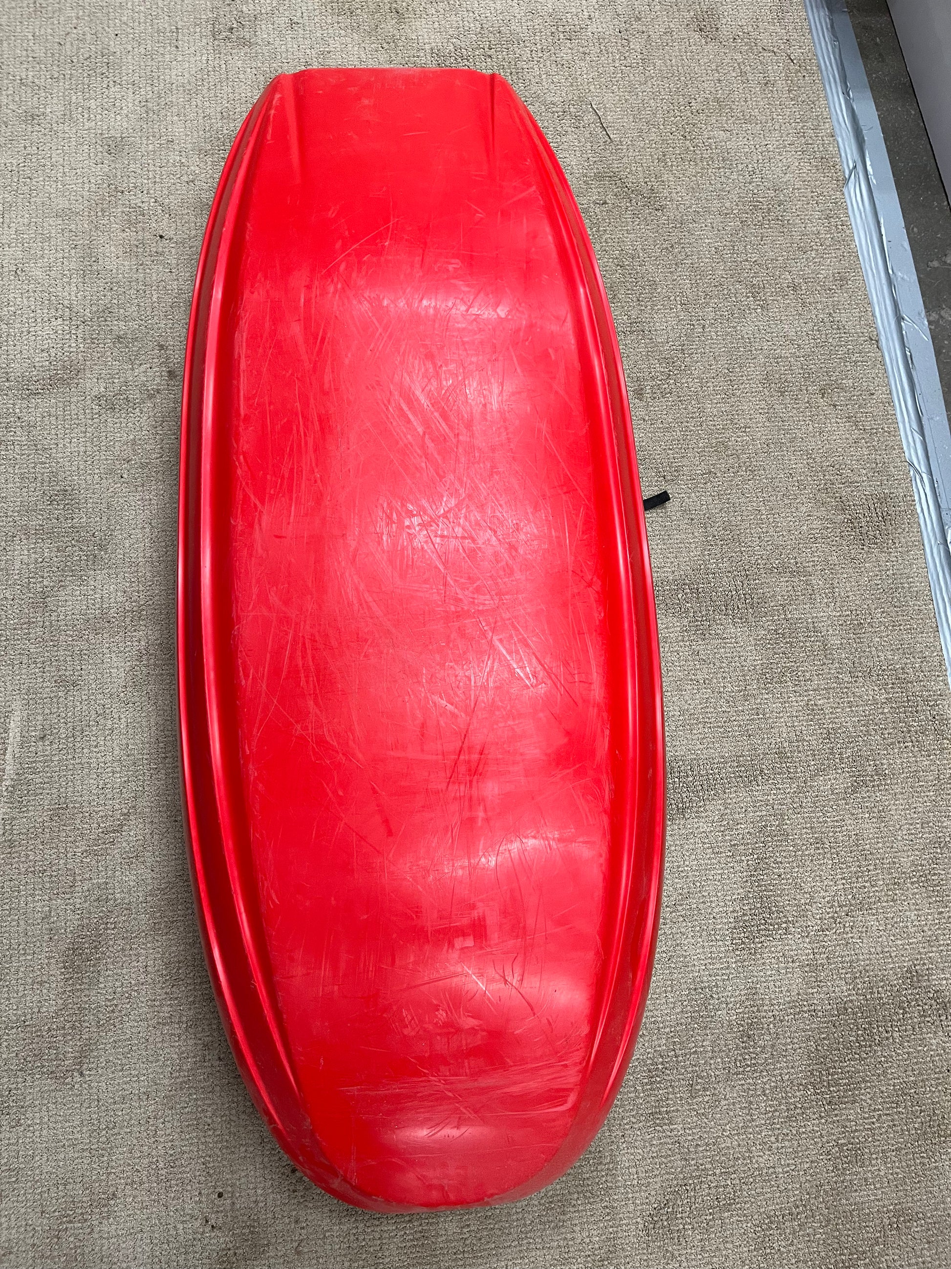 A Jackson Kayak Demo Rockstar V LG with visible scratches lies upside down on a beige carpet next to a metal strip, resembling a used kayak awaiting its next adventure.