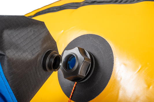 Close-up of a Flextail Pump / Inflation Bag Adapter by Alpacka on a yellow inflatable, showing a black cap with surrounding black and blue material, compatible with TAV adapters for use with mini inflator pumps.