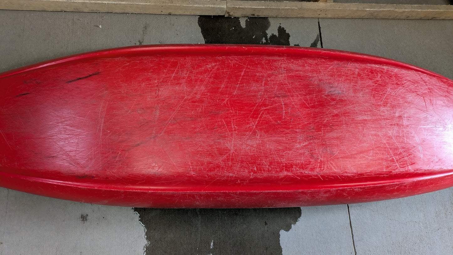 A red Jackson Kayak Demo Clutch 2025, used and scratched, sits upside down on concrete with a wet patch beneath it.