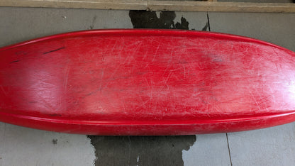 A red Jackson Kayak Demo Clutch 2025, used and scratched, sits upside down on concrete with a wet patch beneath it.