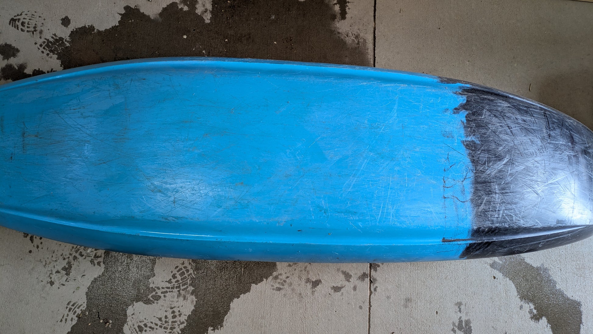 A blue surfboard lies face down on a concrete floor, its nose marked by a black patch—similar to the wear seen on a well-used Demo Gnarvana MD from Jackson Kayak.