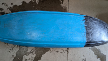 A blue surfboard lies face down on a concrete floor, its nose marked by a black patch—similar to the wear seen on a well-used Demo Gnarvana MD from Jackson Kayak.