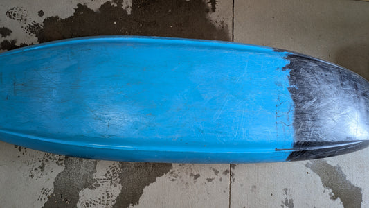 A blue surfboard lies face down on a concrete floor, its nose marked by a black patch—similar to the wear seen on a well-used Demo Gnarvana MD from Jackson Kayak.