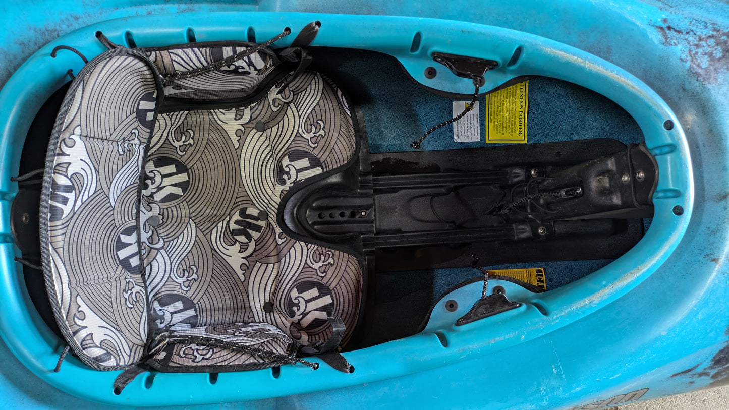 Close-up of the seat and footrest inside a blue Demo Gnarvana MD by Jackson Kayak, featuring patterned seat padding and adjustment mechanisms from our demo fleet.