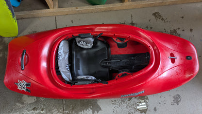 A red used Jackson Kayak Demo Rockstar V LG is upright on a wet concrete floor, displaying the cockpit and seat from above.
