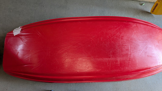 A red plastic Demo Rockstar V LG from Jackson Kayak, with visible scratches and a torn white label, sits upside down on a concrete floor, ready for its next adventure.