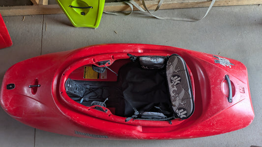 A Jackson Kayak Demo Rockstar V MD with a patterned seat cushion and footrests, seen from above on concrete beside a green paddle blade—this used kayak is adventure-ready.