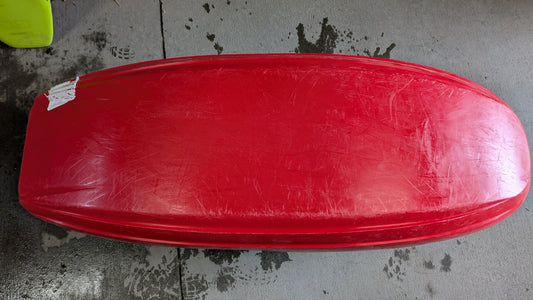A Jackson Kayak Demo Rockstar V SM in red is upside down on wet concrete, displaying visible scratches and a small white tape patch at one end.