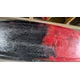 Close-up of the scratched hull of a Jackson Kayak Demo Clutch 2025, featuring worn black and red paint; wooden shelves and paddles are partially visible in the background.