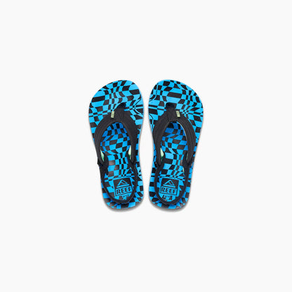 A pair of REEF LITTLE AHI children's flip-flops with black straps and blue and black geometric checkered soles, featuring a durable foam outsole, shown on a white background.