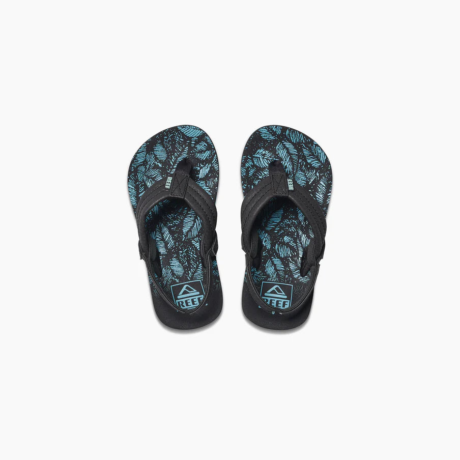 A pair of REEF LITTLE AHI children's flip flops in black with blue and black leaf-patterned insoles, featuring the REEF logo on the heel and a durable foam outsole, shown from above on a white background.