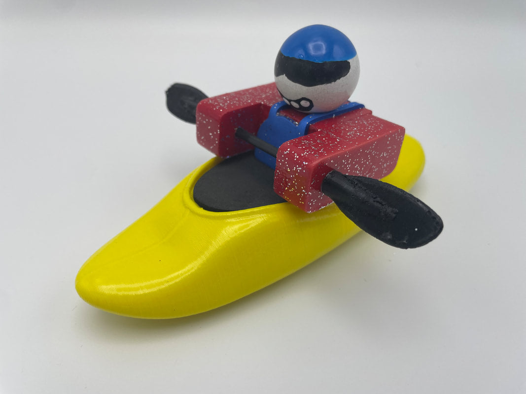The Foamie Friends' Foamie Mini Playboat showcases a toy figure in a yellow kayak with an impressive hull design, complete with a red life vest, blue helmet, and black paddle against a plain background.