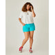 A person with curly hair exudes confidence in a vacation outfit against a plain background, wearing a white shirt, Carve's Oahu 4" turquoise shorts, and red sneakers, gazing at the camera while stylishly tousling their hair with one hand.