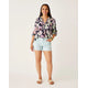 A person in a floral blouse and Carve's Oahu 4" Shorts from their vacation wardrobe stands against a plain background.