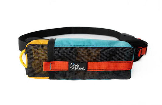 The GuideLaunch Waist Throw Bag by River Station Gear is rectangular, with teal, yellow, and black colors, a red strap, the "River Station" label on front, and features a floating rescue rope. Shown on a white background.