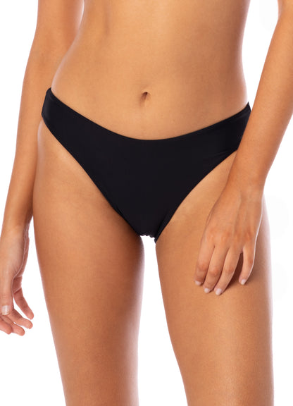 A person wearing Maaji’s Sublimity Bikini black low rise bottoms—pictured from mid-torso to upper thighs—with one arm relaxed at their side.
