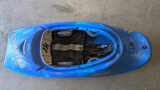 A Consignment Medium Jackson Rockstar 3.0 freestyle kayak from 4Corners Riversports sits on a concrete floor, viewed from above, highlighting its cockpit and seat details.