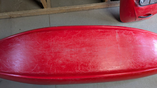 A used red Jackson Kayak Demo Flow SM with visible scratches and wear is shown from above, resting on a concrete floor next to a wooden frame.