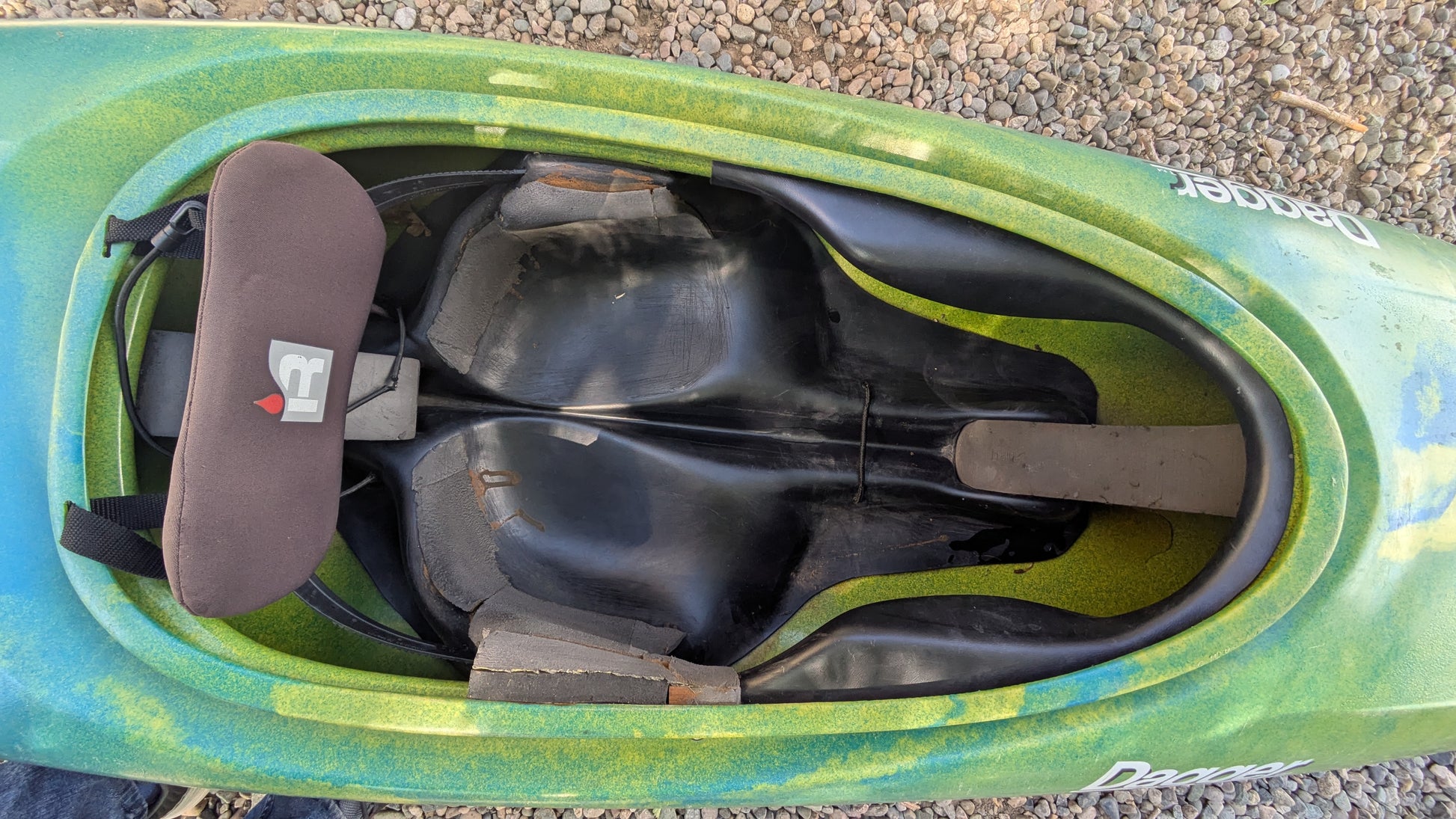 Top view of a barely used, nearly virgin Dagger Sawblade Outburst from 4Corners Riversports, showing the seat, backrest, footrest, and interior plastic with gravel visible outside the kayak.