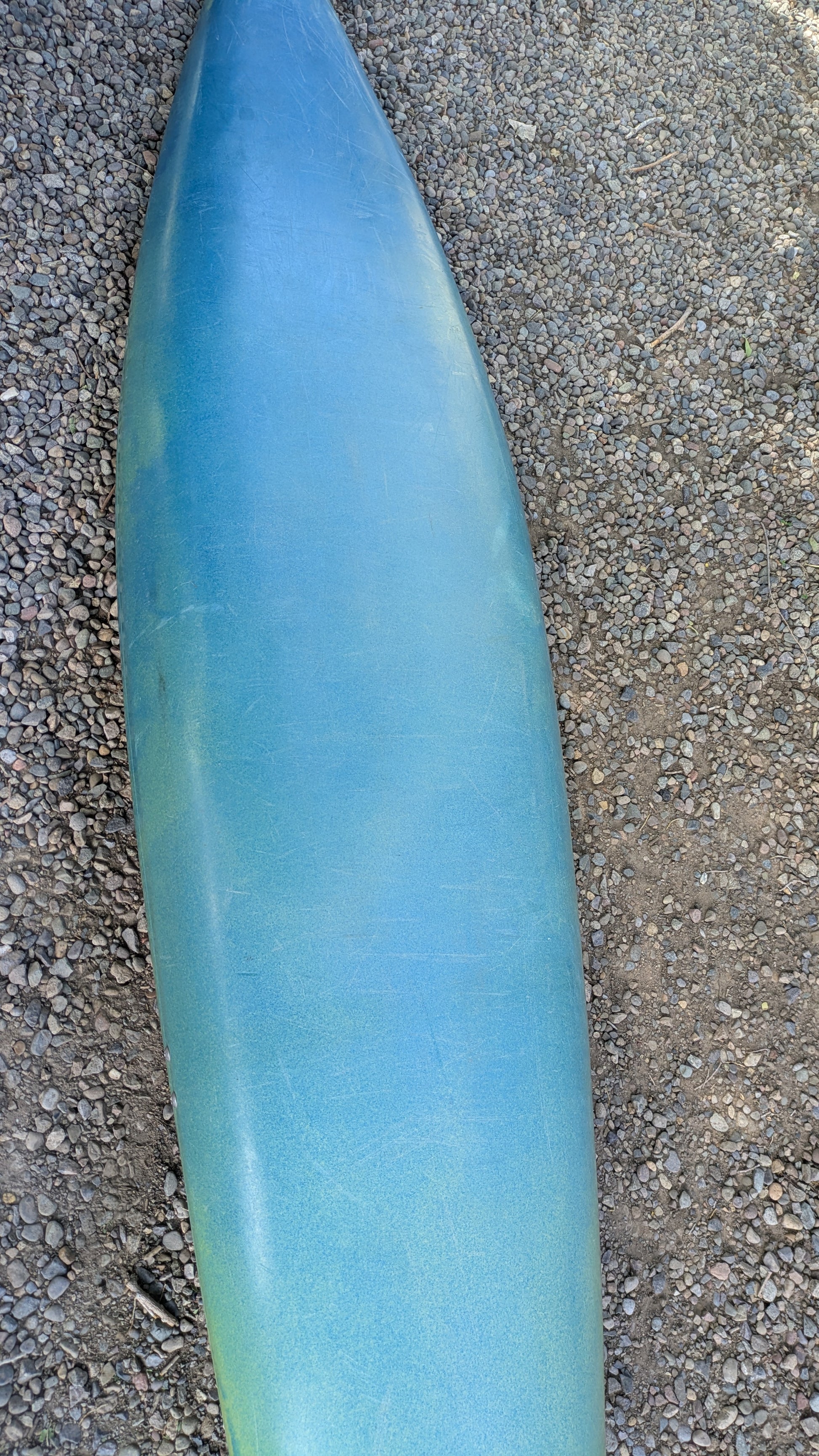 A barely used, nearly virgin Dagger Sawblade Outburst kayak from 4Corners Riversports is lying face down on a gravel and dirt surface.