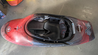 A red 4CRS Consignment Rockstar 4.0 freestyle kayak rests upside down on a concrete floor, displaying its open cockpit and black seat interior.