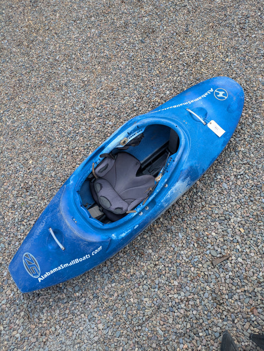 A blue Consignment Wavesport ZG kayak by Wavesport sits on gravel, featuring a padded seat and "AlabamaSmallBoats.com" printed on the side.