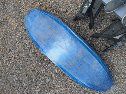 A blue, scratched Consignment Wavesport ZG kayak from Wavesport rests on gravel beside a black folding chair and part of a gray shoe.
