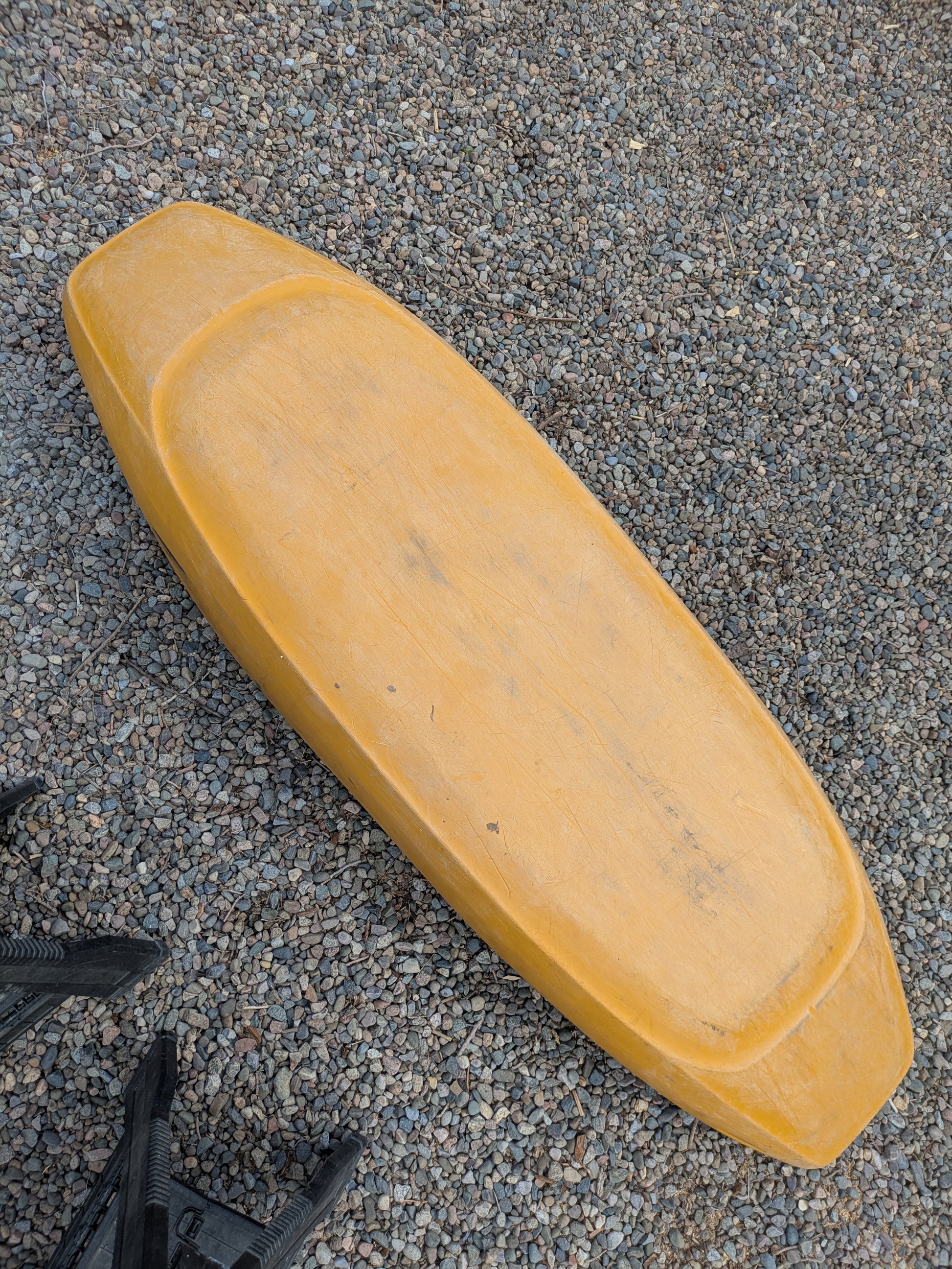 A yellow, rectangular seat cushion with rounded edges lies on gravel, evoking the comfort of a Wavesport Consignment LiquidLogic CR125 kayak.