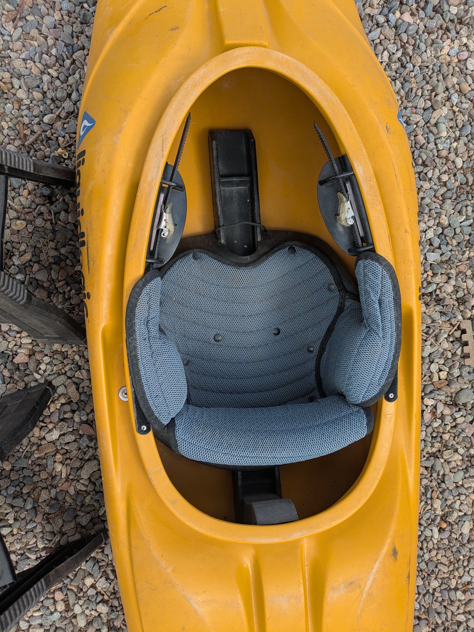 Top view of a Consignment LiquidLogic CR125 river runner kayak by Wavesport, featuring a padded blue seat and set on gravel.