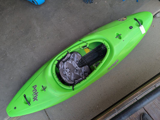 A Jackson Kayak Consignment Antix 2.0 L whitewater kayak with a patterned seat cushion and paddle holder sits indoors on a concrete floor.