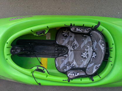 Top view of the Consignment Jackson Antix 2.0 L by Jackson Kayak, featuring empty padded seat, footrests, and black bungee cords on concrete—ideal for exciting river-running adventures.