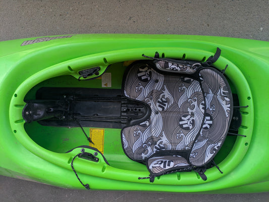 Top view of the Consignment Jackson Antix 2.0 L by Jackson Kayak, featuring empty padded seat, footrests, and black bungee cords on concrete—ideal for exciting river-running adventures.