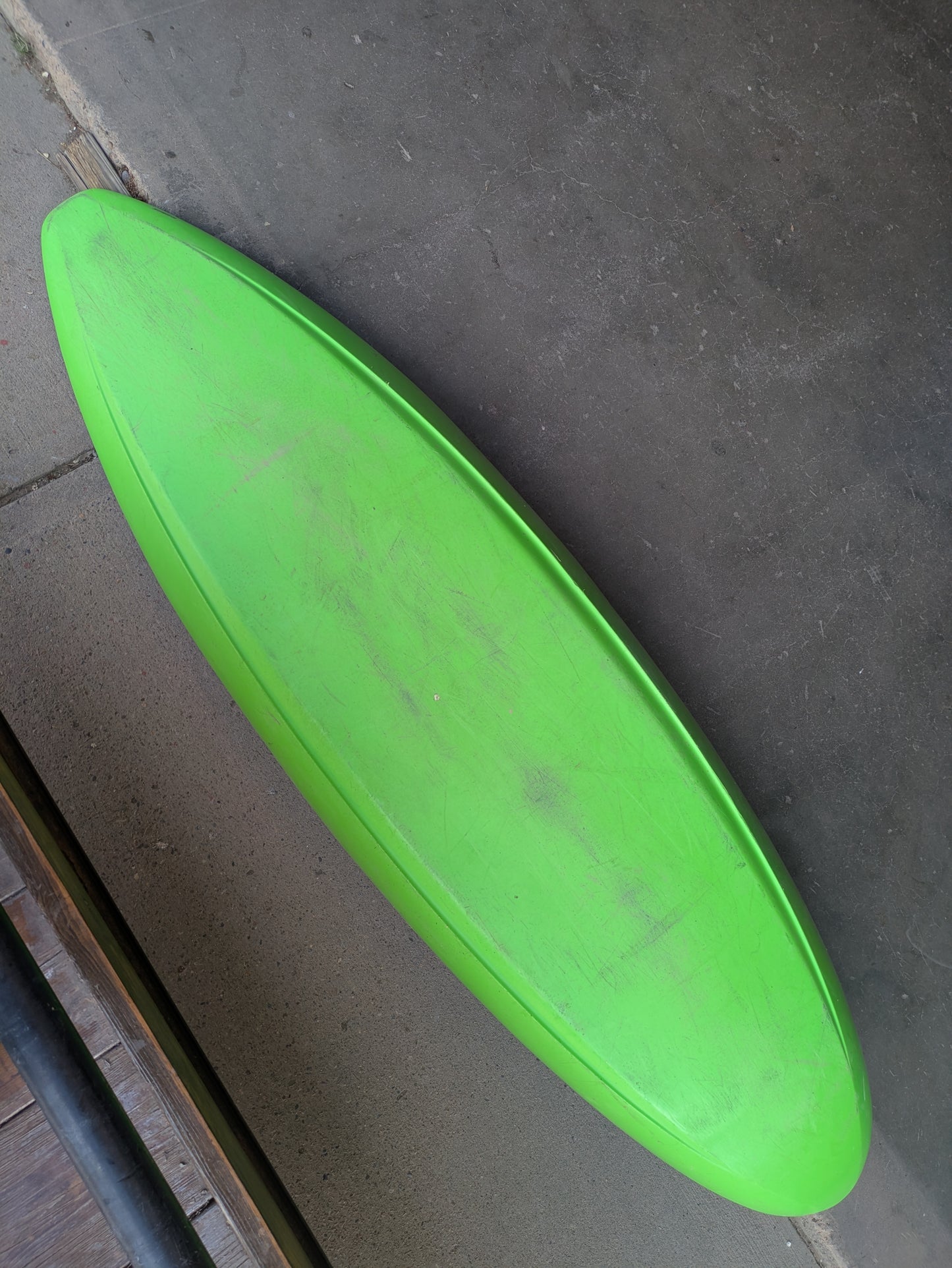 A Consignment Jackson Antix 2.0 L whitewater kayak by Jackson Kayak in green rests flat on a concrete floor, seen from above at an angle.