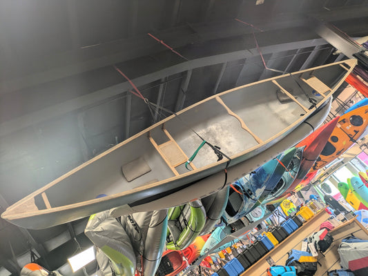 A Dagger Venture 17 canoe by Dagger, ideal for tandem expeditions, hangs from the store ceiling with kayaks and equipment showcased in the background.