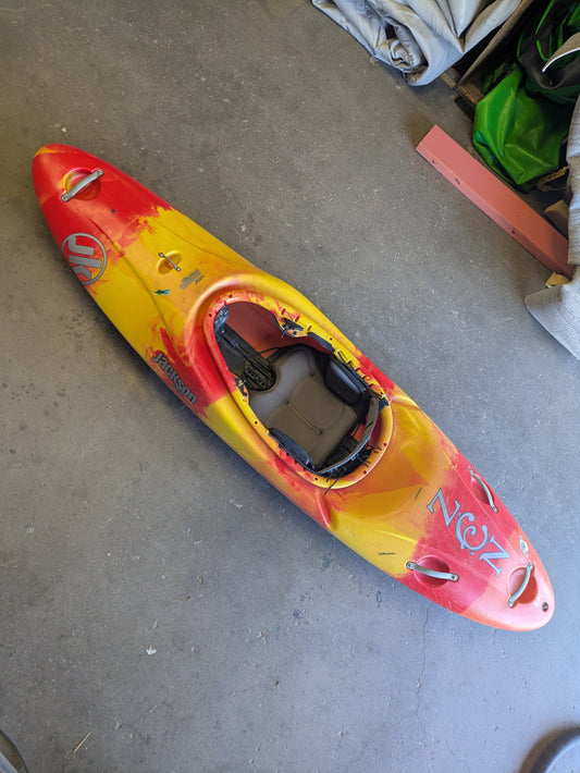 A Used Jackson Zen by Jackson Kayak, featuring a red and yellow design and padded seat, is placed on a concrete floor in a garage or storage area.
