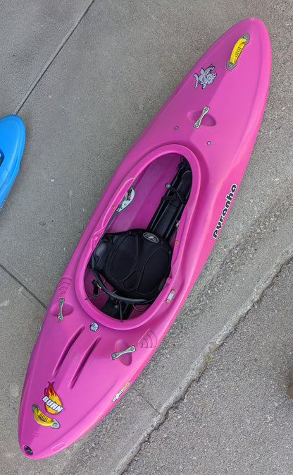 The 4Corners Riversports Consignment Pyranha Burn 1 - Small Pink kayak, featuring black seat fittings and cartoon decals, is placed on a concrete surface by the curb—perfect for paddler development.