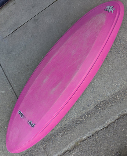 A Consignment Pyranha Burn 1 - Small Pink kayak from 4Corners Riversports lies upside down on concrete, showing signs of use and featuring a small cartoon graphic near the nose.