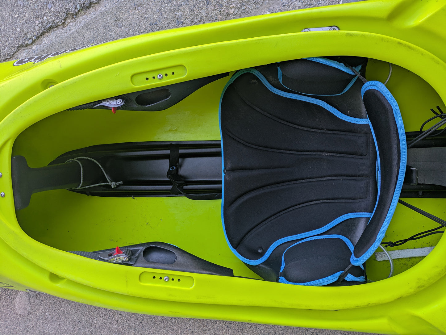 Top-down view of a Consignment Pyranha 9r Large kayak by 4Corners Riversports, featuring a bright green cockpit with padded seat and foot braces, shown resting on concrete.